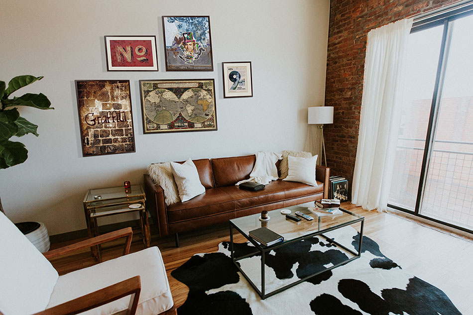 Композиция из постеров в рамах над коричневым кожаным диваном в гостиной в стиле лофт