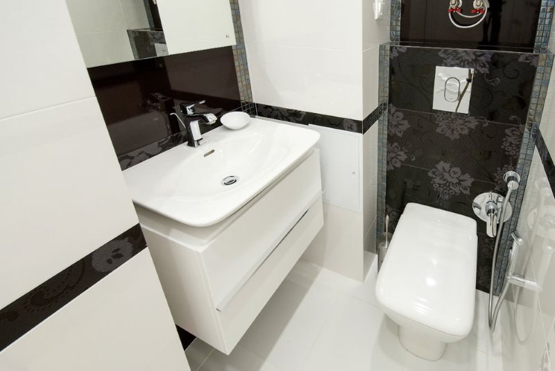 Белая сантехника в туалетной комнате с черной плиткой