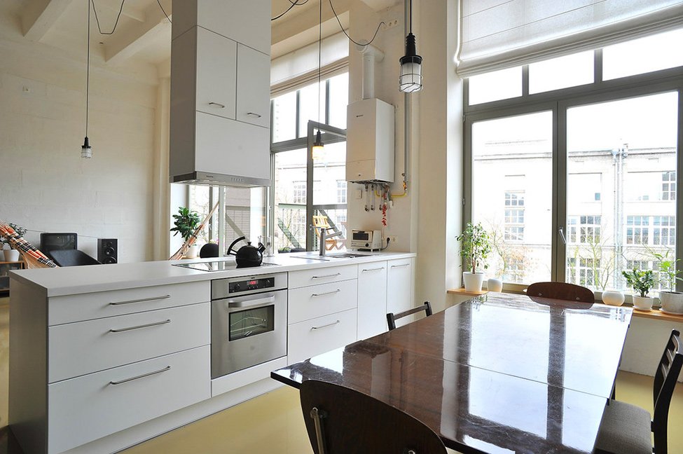 Белая кухонная мебель и тёмный деревянный обеденный стол в лофт-квартире от студии Inblum в Литве