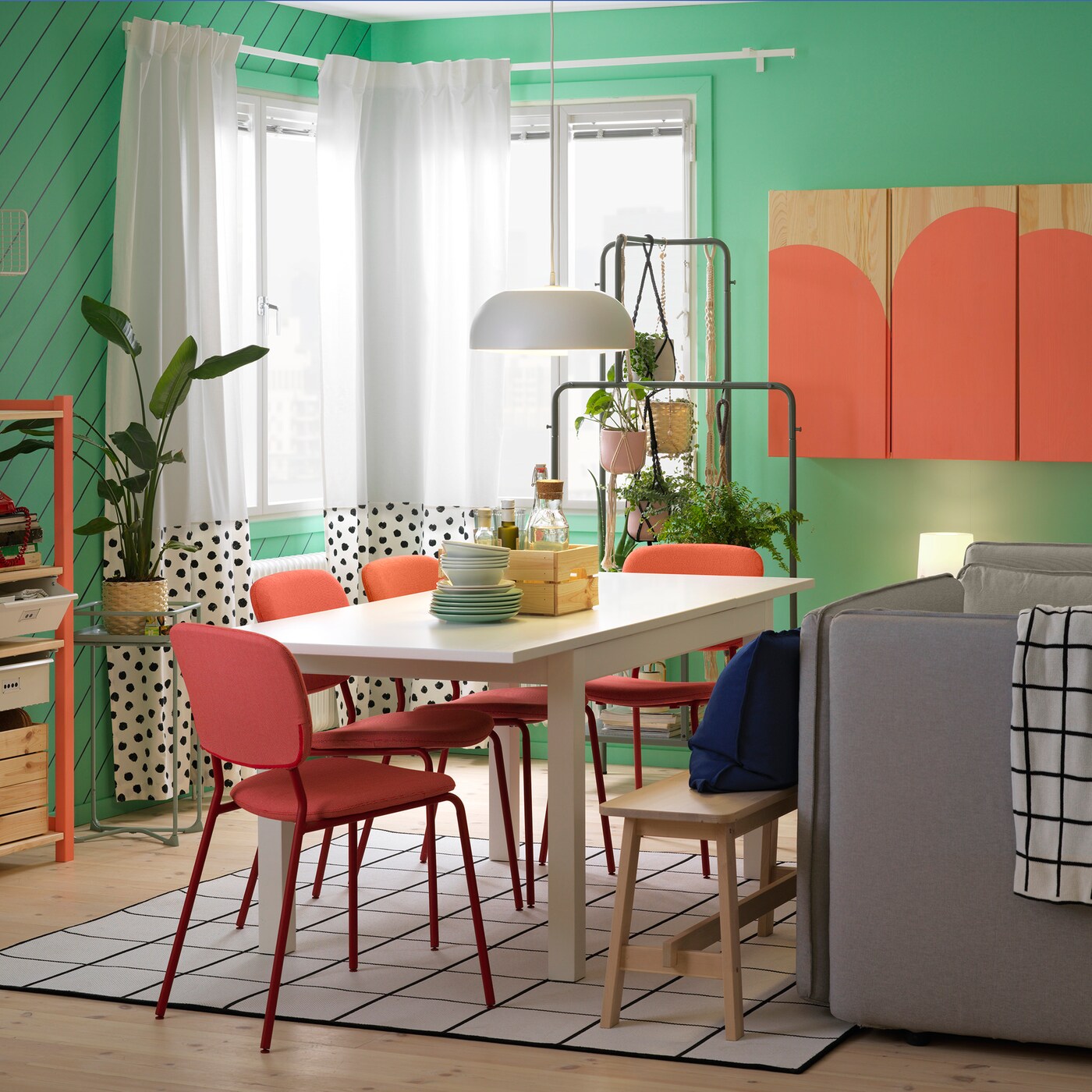 A dining room with a table and chairs, a cabinet with diverse boxes and a window in the background with light curtains.